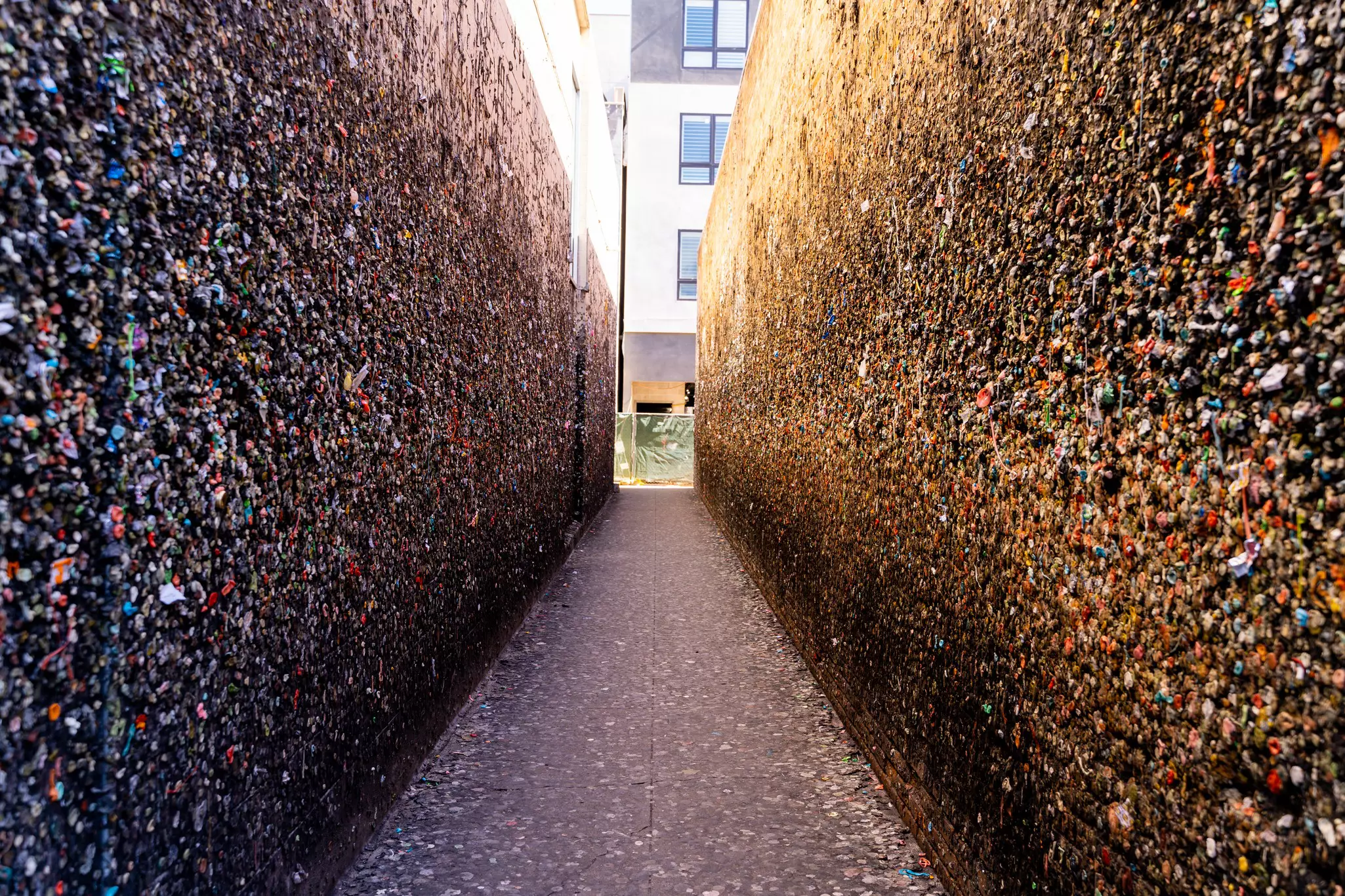 A narrow passage between two tall walls covered with discarded bubble gum.