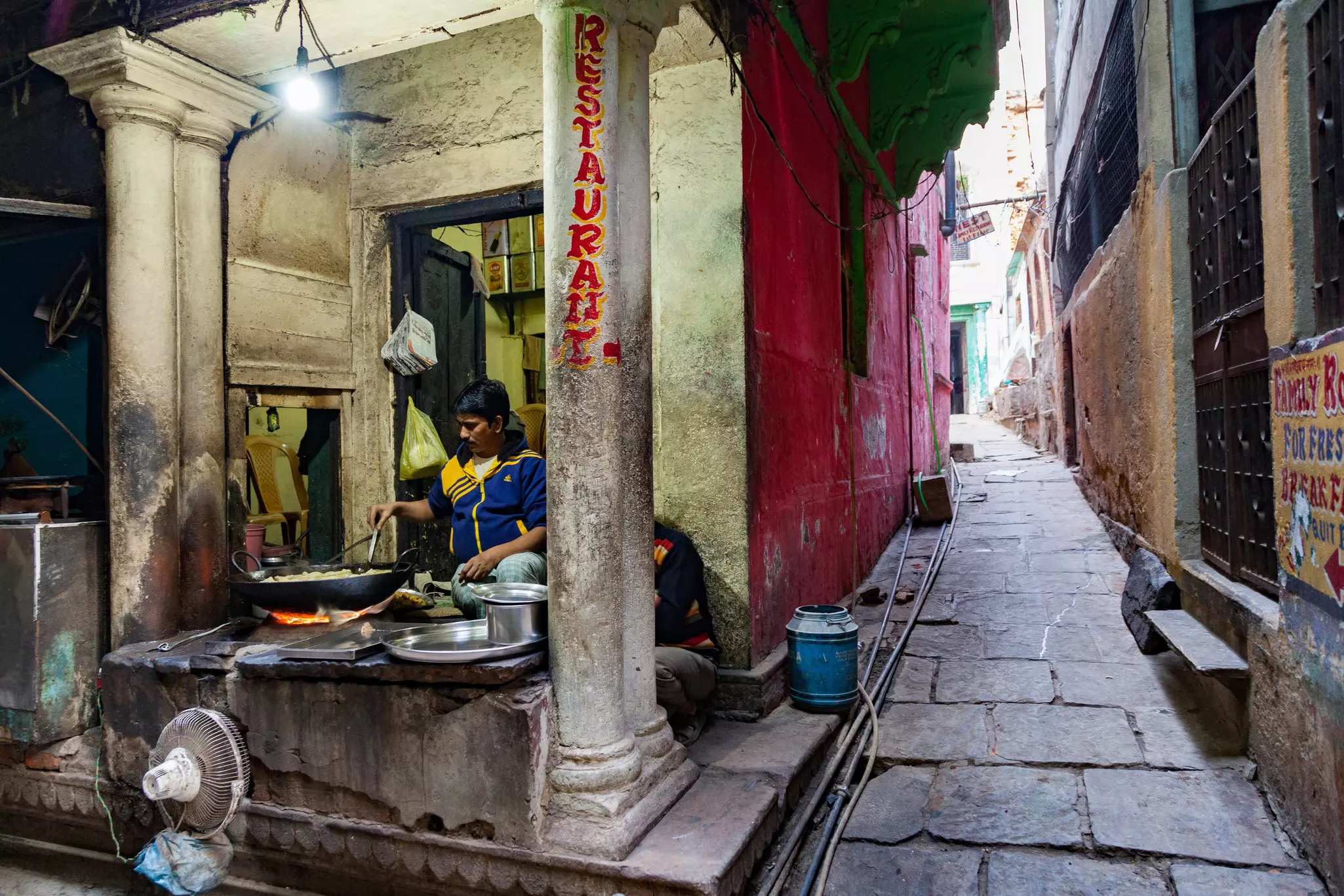 A vendor operates a street food stall on a narrow alley in a historic city.