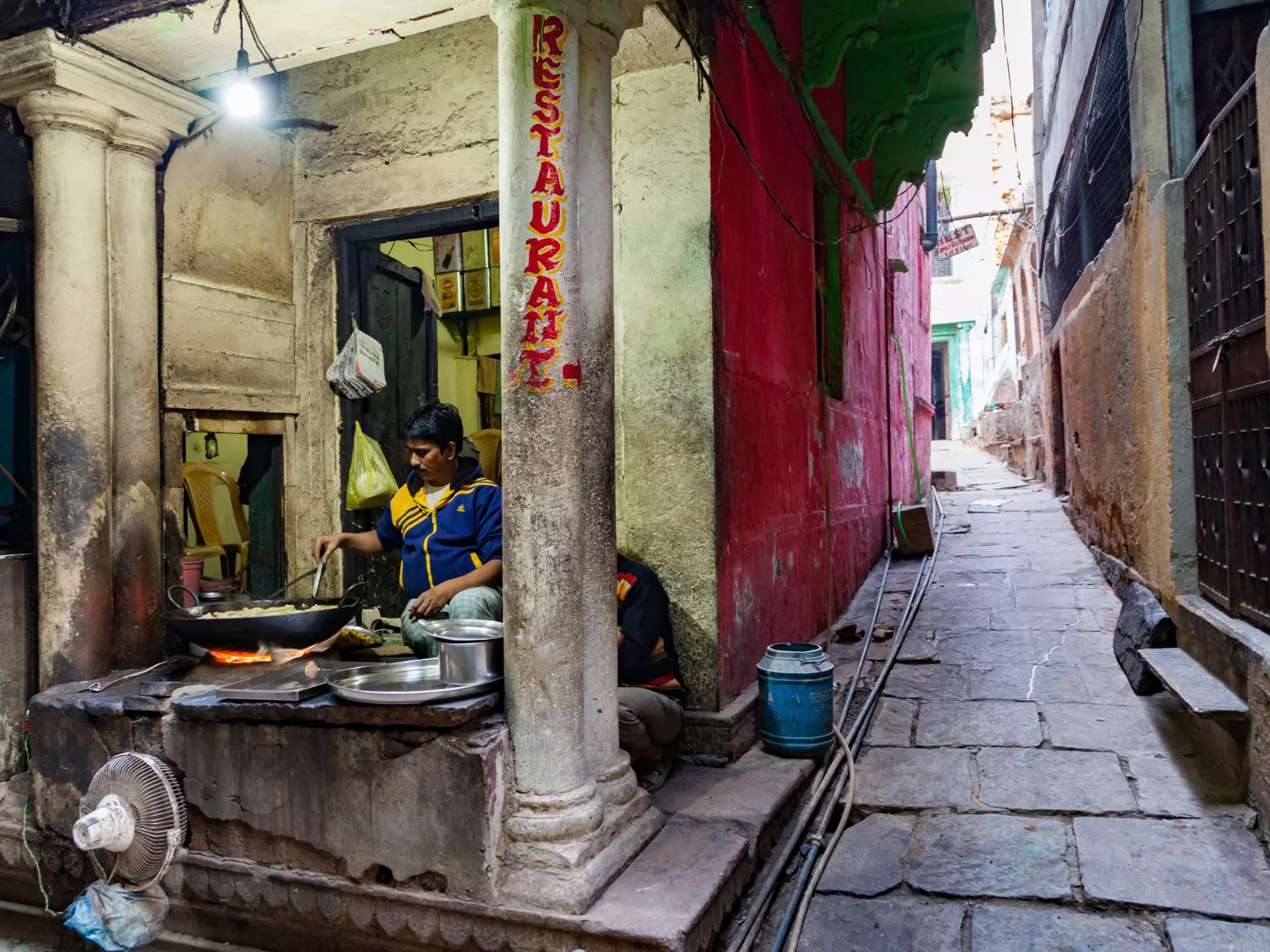 A vendor operates a street food stall on a narrow alley in a historic city.