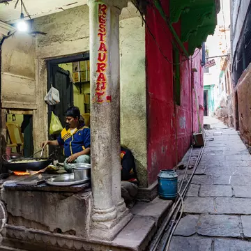A vendor operates a street food stall on a narrow alley in a historic city.