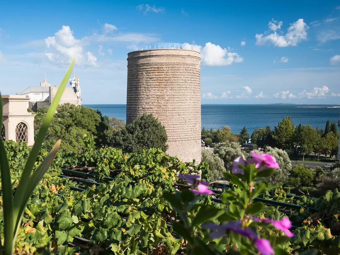 A view of the UNESCO World Heritage listed Maiden's Tower, trees in the foreground with the Caspian Sea in the background, Baku, Azerbaijan.