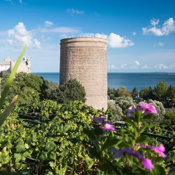 A view of the UNESCO World Heritage listed Maiden's Tower, trees in the foreground with the Caspian Sea in the background, Baku, Azerbaijan.
