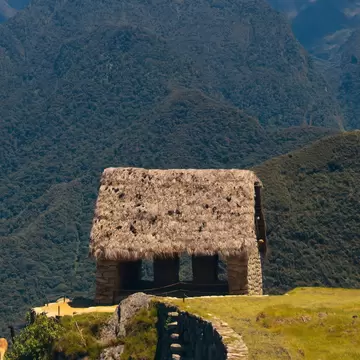 Ruins of the Hut of the Caretaker of the Funerary Rock against green mountains in Machu Picchu, Peru.