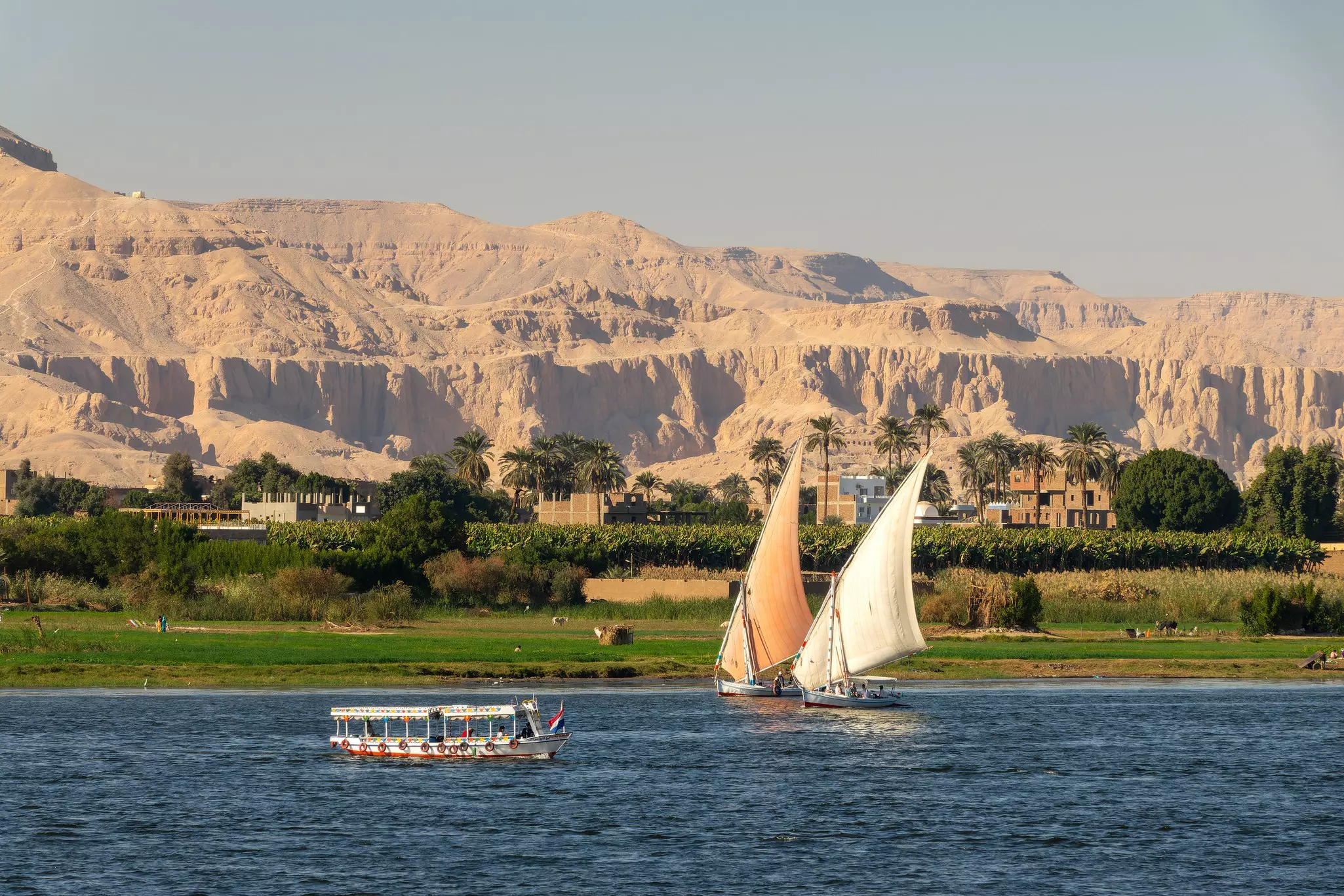 Two sailboats with another boat on a lake with green trees and mountains in the background round