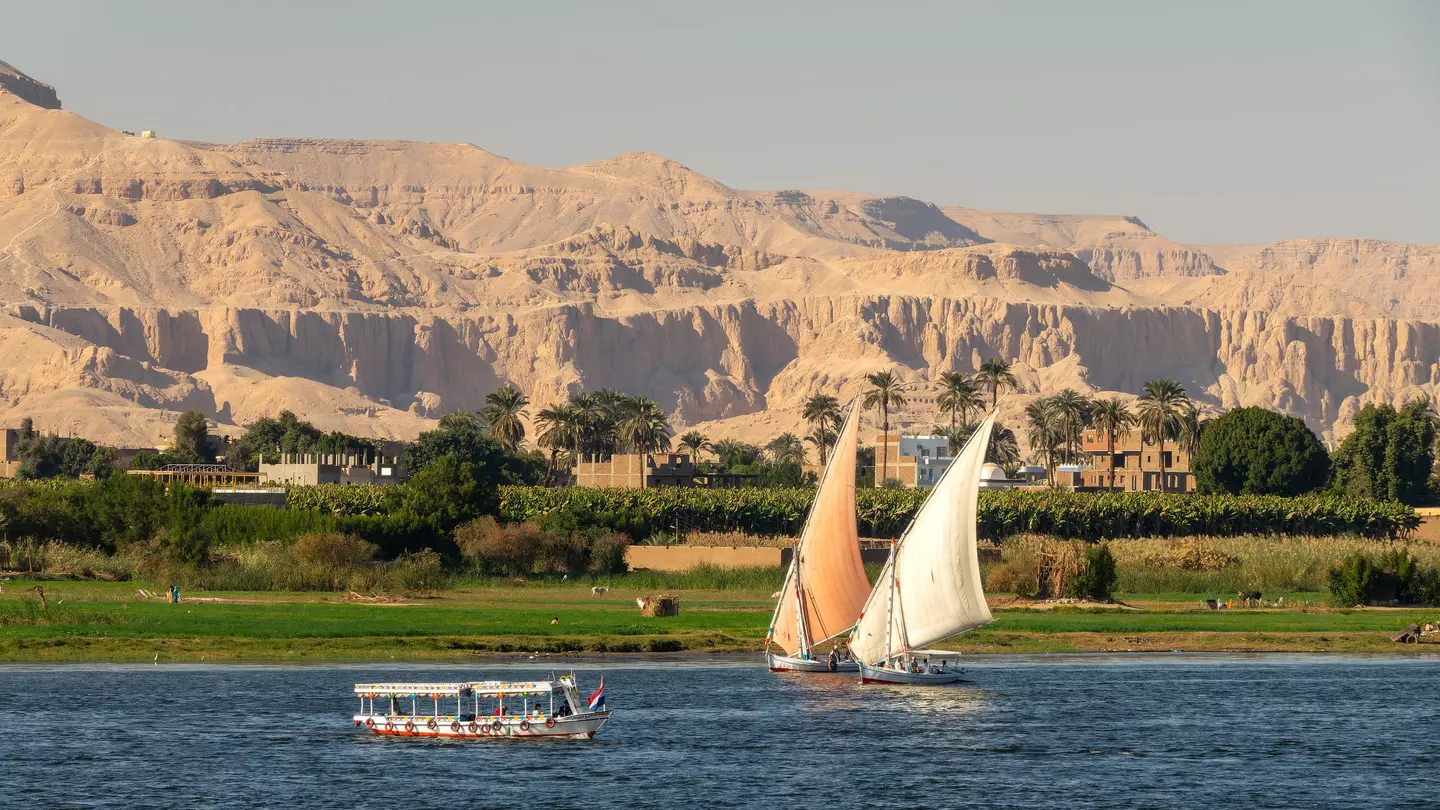 Two sailboats with another boat on a lake with green trees and mountains in the background round