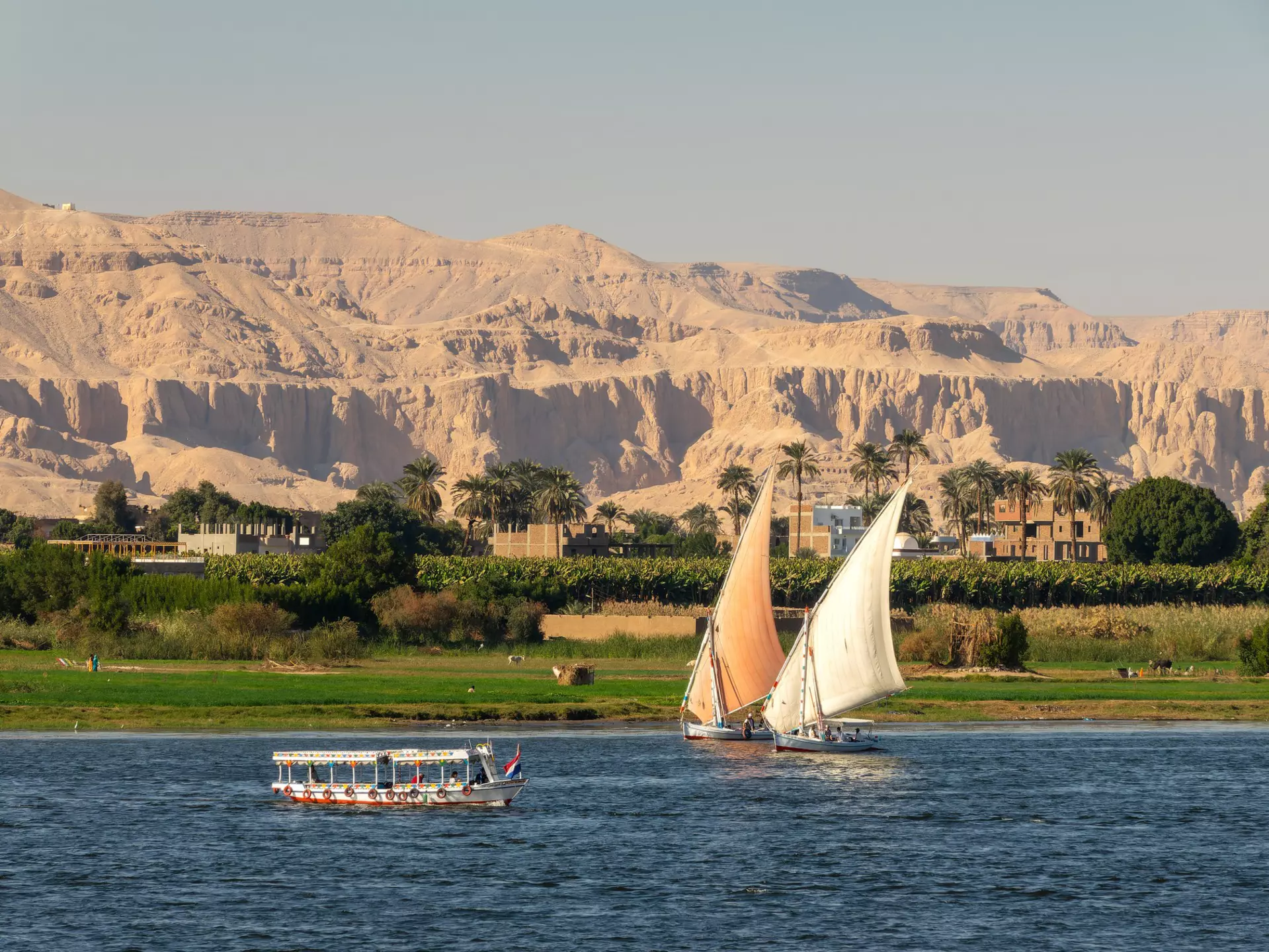 Two sailboats with another boat on a lake with green trees and mountains in the background round