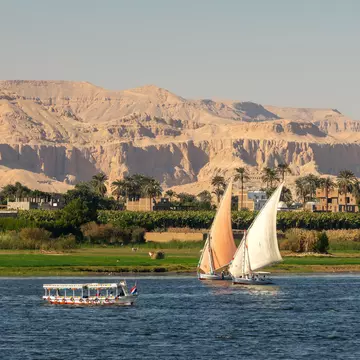 Two sailboats with another boat on a lake with green trees and mountains in the background round