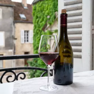 A bottle of red wine and wine glass on a table near a balcony of a historic French building