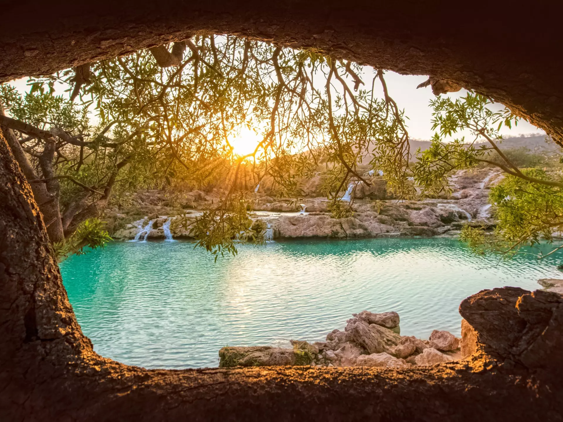 Sun shining through trees onto a waterfall and river