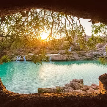 Sun shining through trees onto a waterfall and river