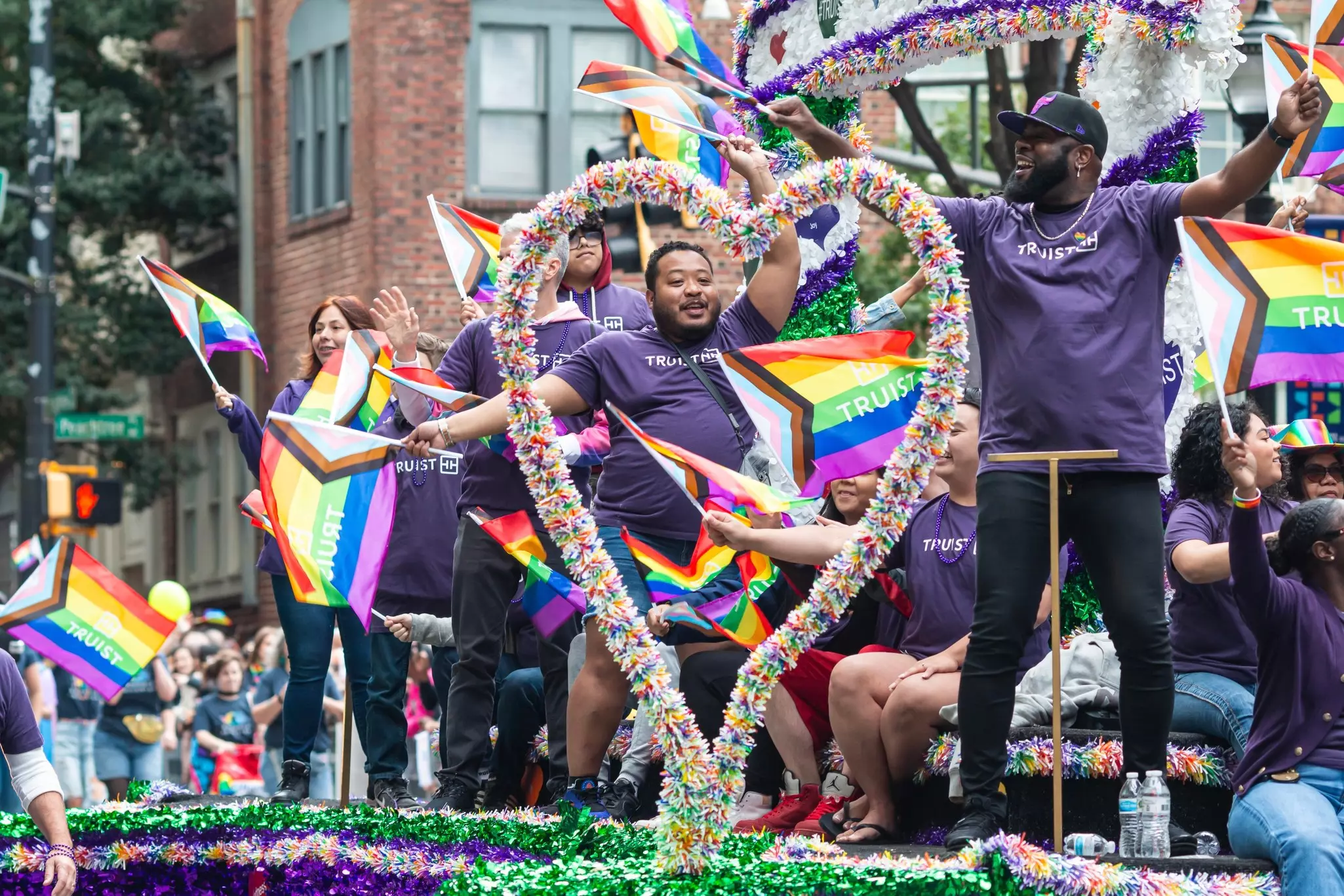 People dance and wave rainbow flags atop a float during a parade.