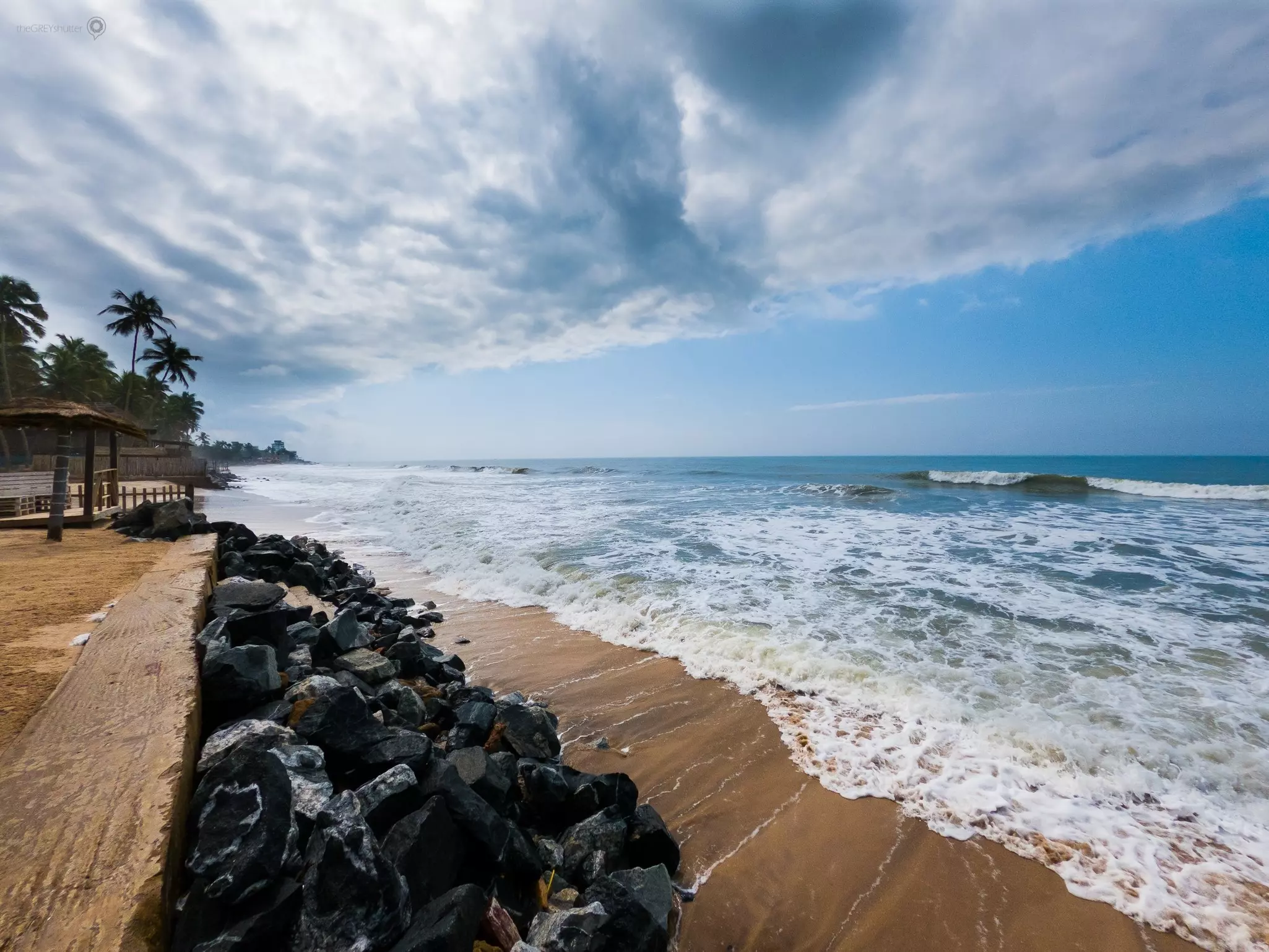 The ocean laps on a sandy shore with dark boulders on a cloudy day