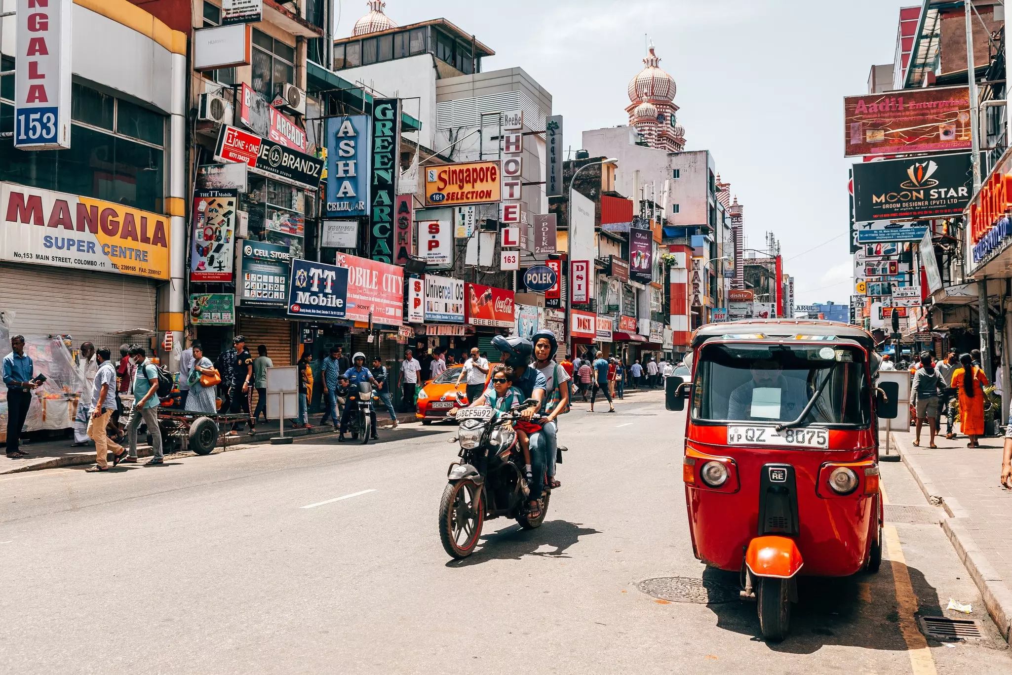 People on a busy street in a city with motorcylces and a red tuk tuk.