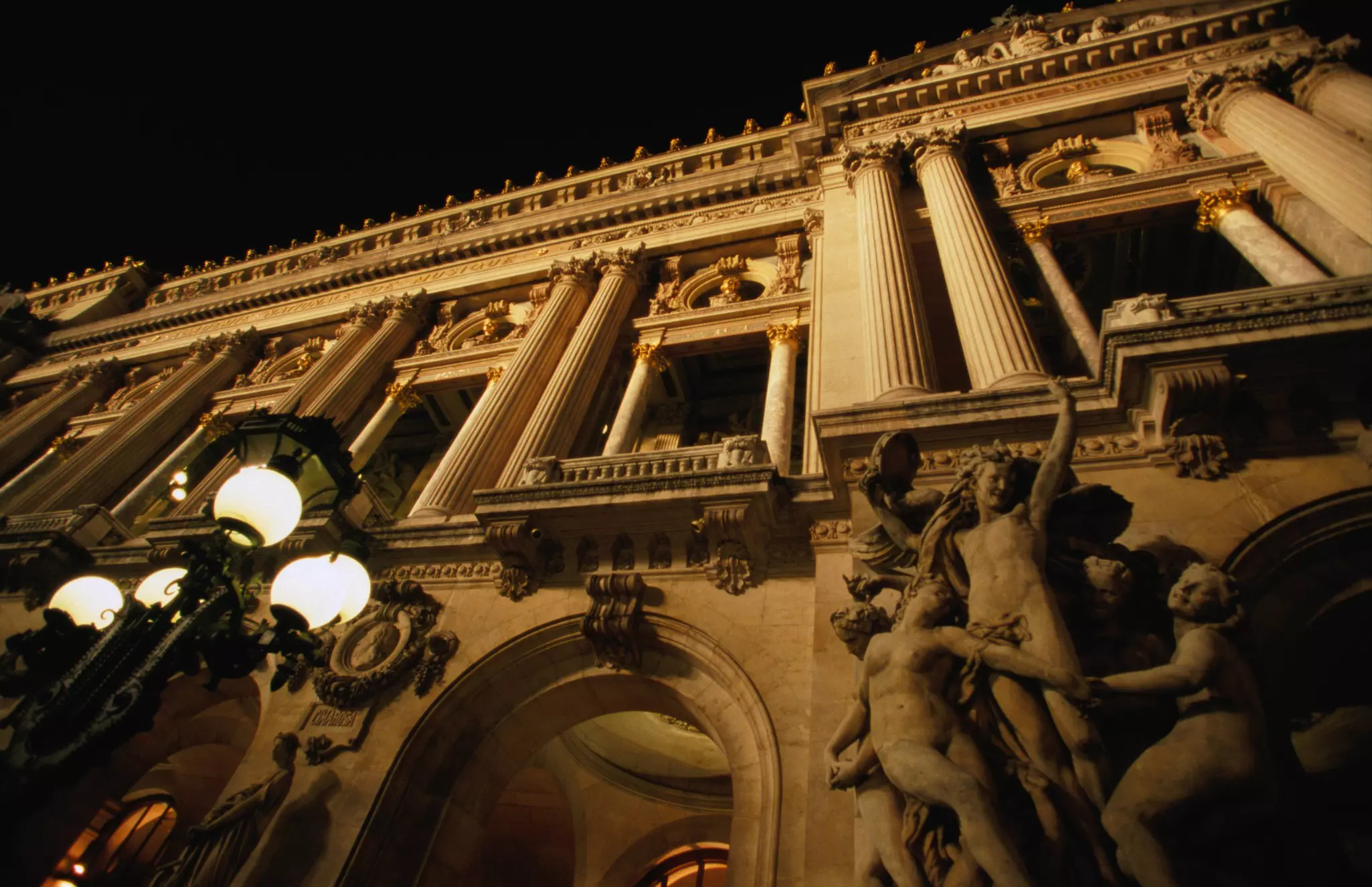 Two figures in shadow walk down a path lined with buildings.