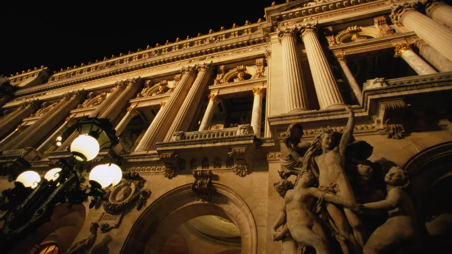 Two figures in shadow walk down a path lined with buildings.
