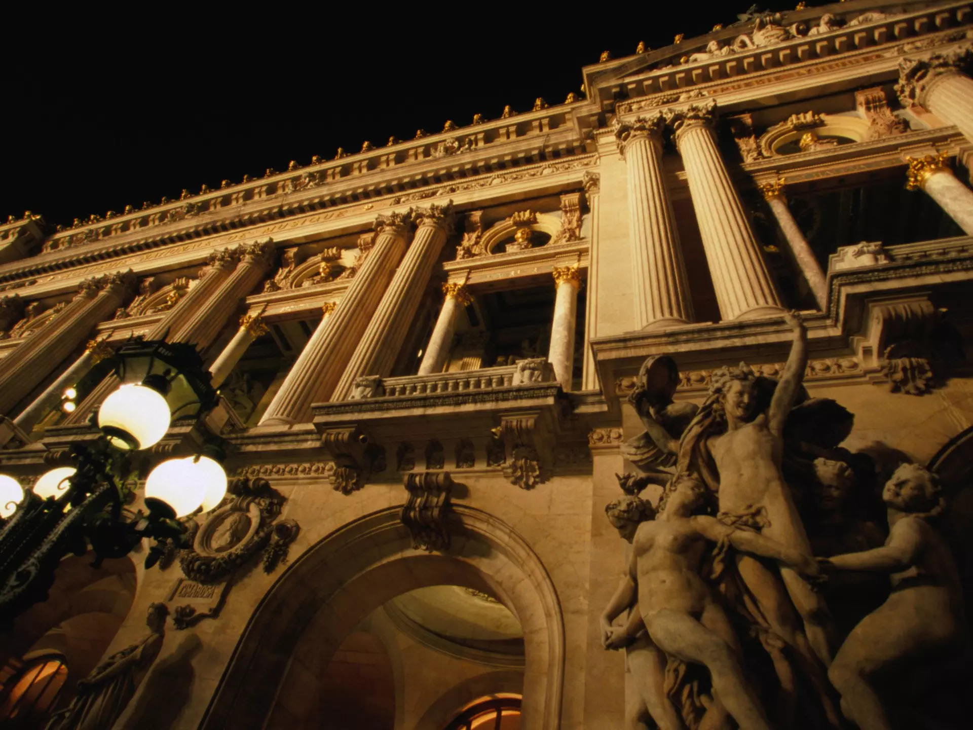 Two figures in shadow walk down a path lined with buildings.