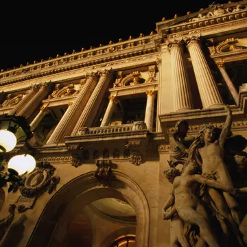 Two figures in shadow walk down a path lined with buildings.