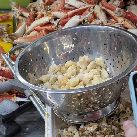 Crab meat in a collander and crab legs in a bin behind it.