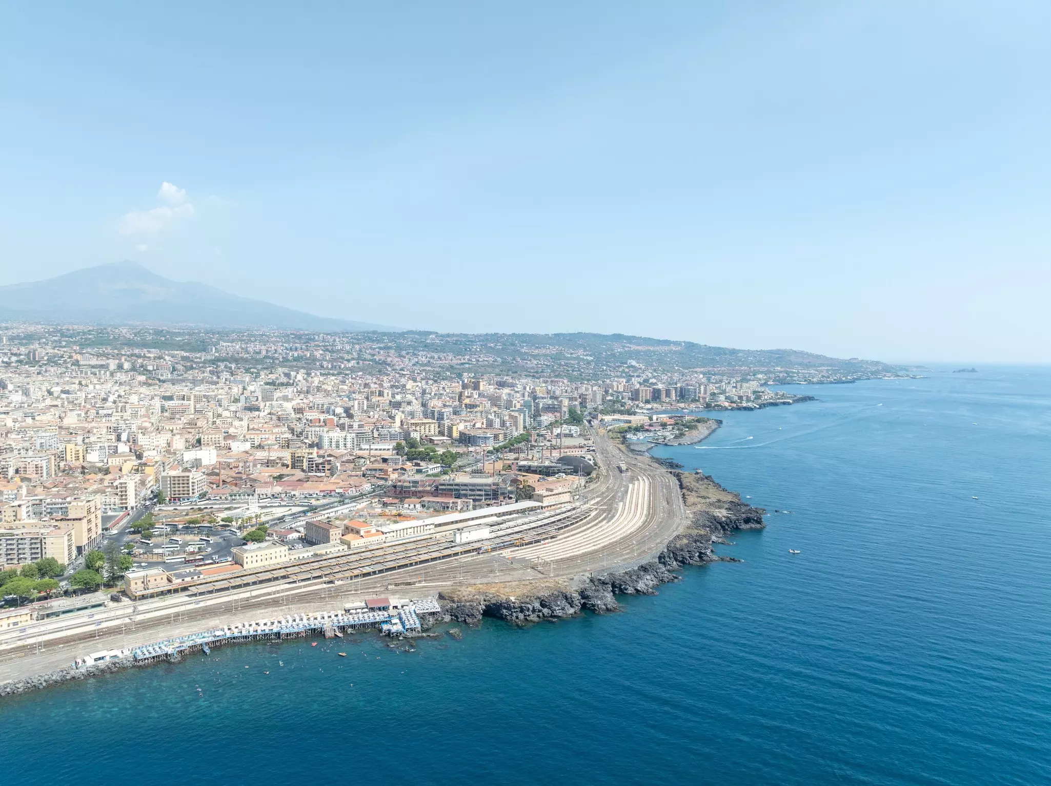 Rail lines along a coast, with a dense town on one side and blue sea on the other.