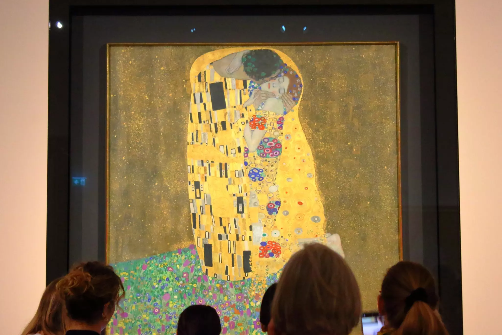People look at a painting depicting two people kissing. The figures are adorned with gold leaf.