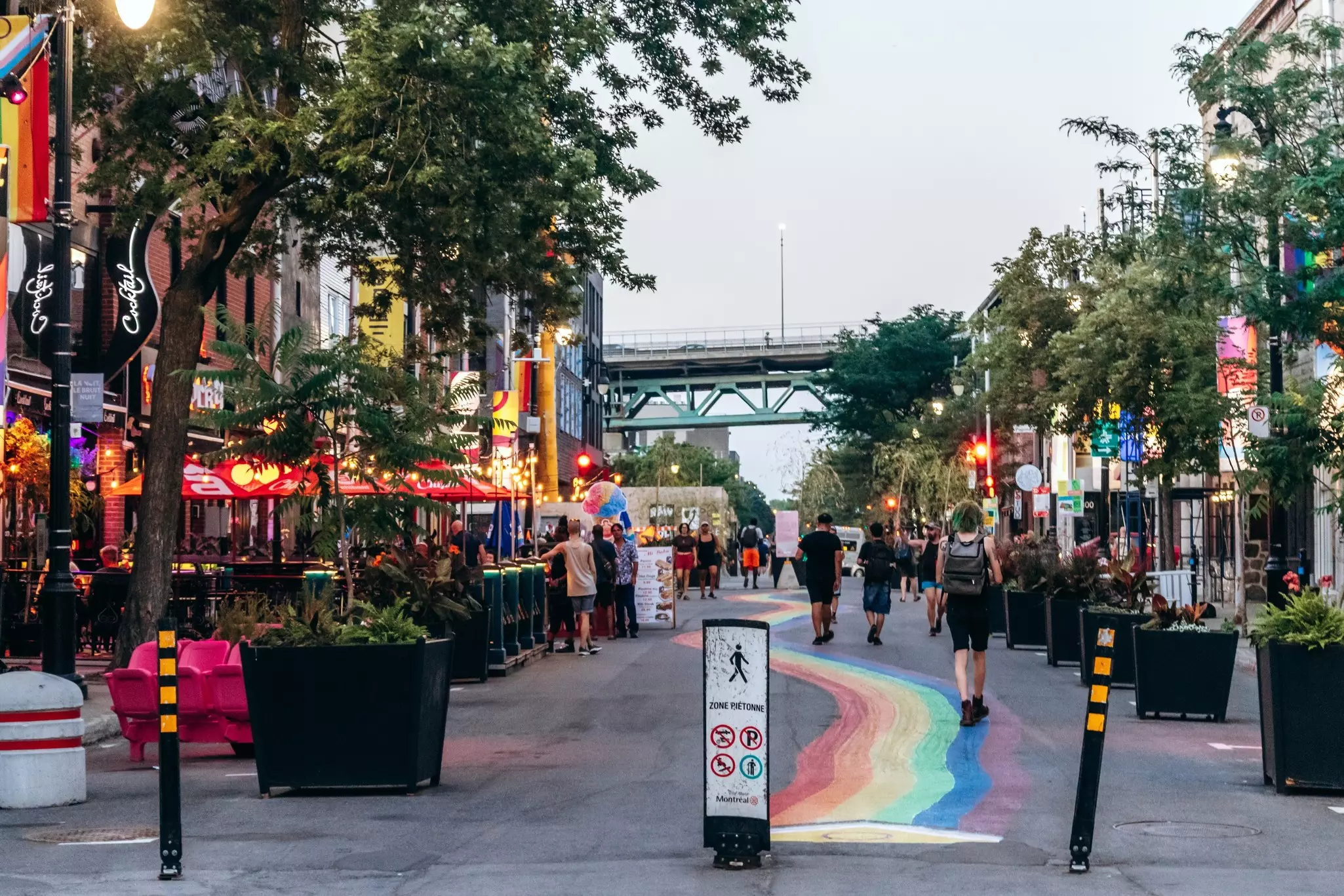 A rainbow is painted on the sidewalk down a street lined with bars