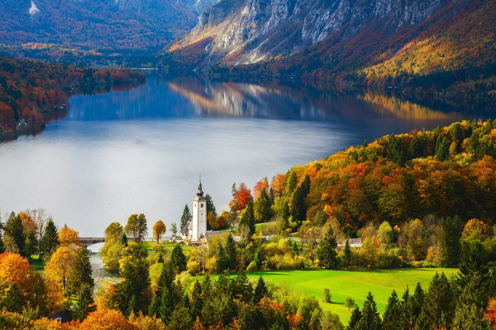 A building with a white steeple by a lake surrounded by mountains.