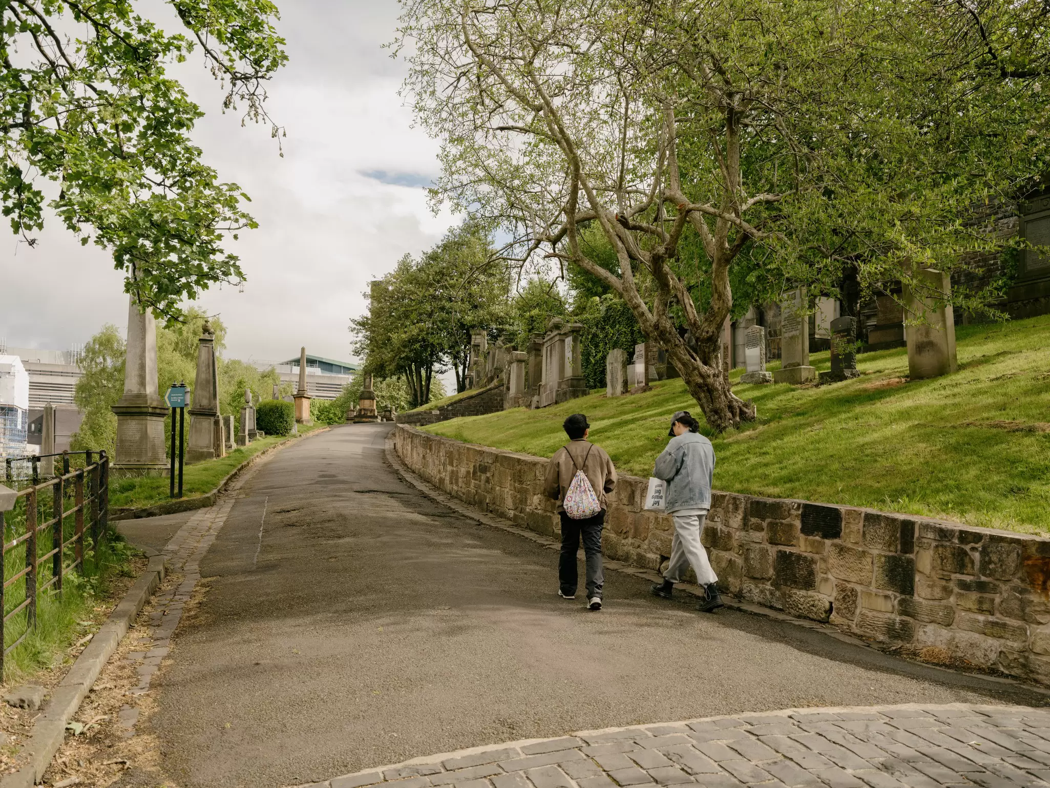 Two people walk along a path in a large cemetery: Glasgow Necropolis