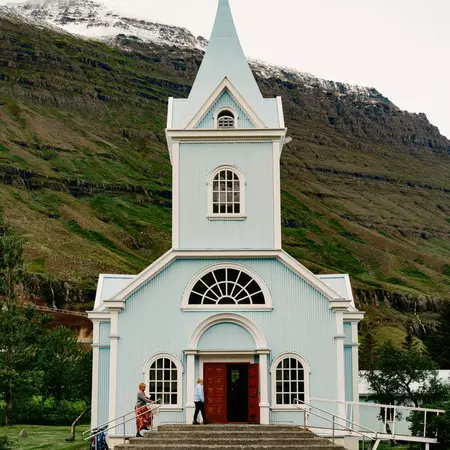 A light blue church with a steeple and a red door.