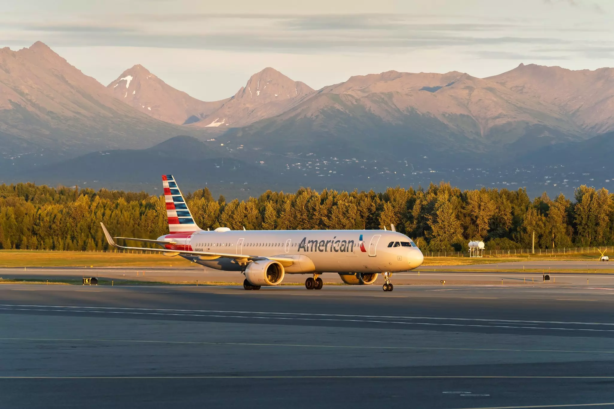 American Airlines aircraft taxing at Ted Stevens Anchorage International Airport with mountains and dusk sky behind