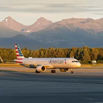 An American Airlines aircraft taxiing at Ted Stevens Anchorage International Airport, with tall mountains in the distance