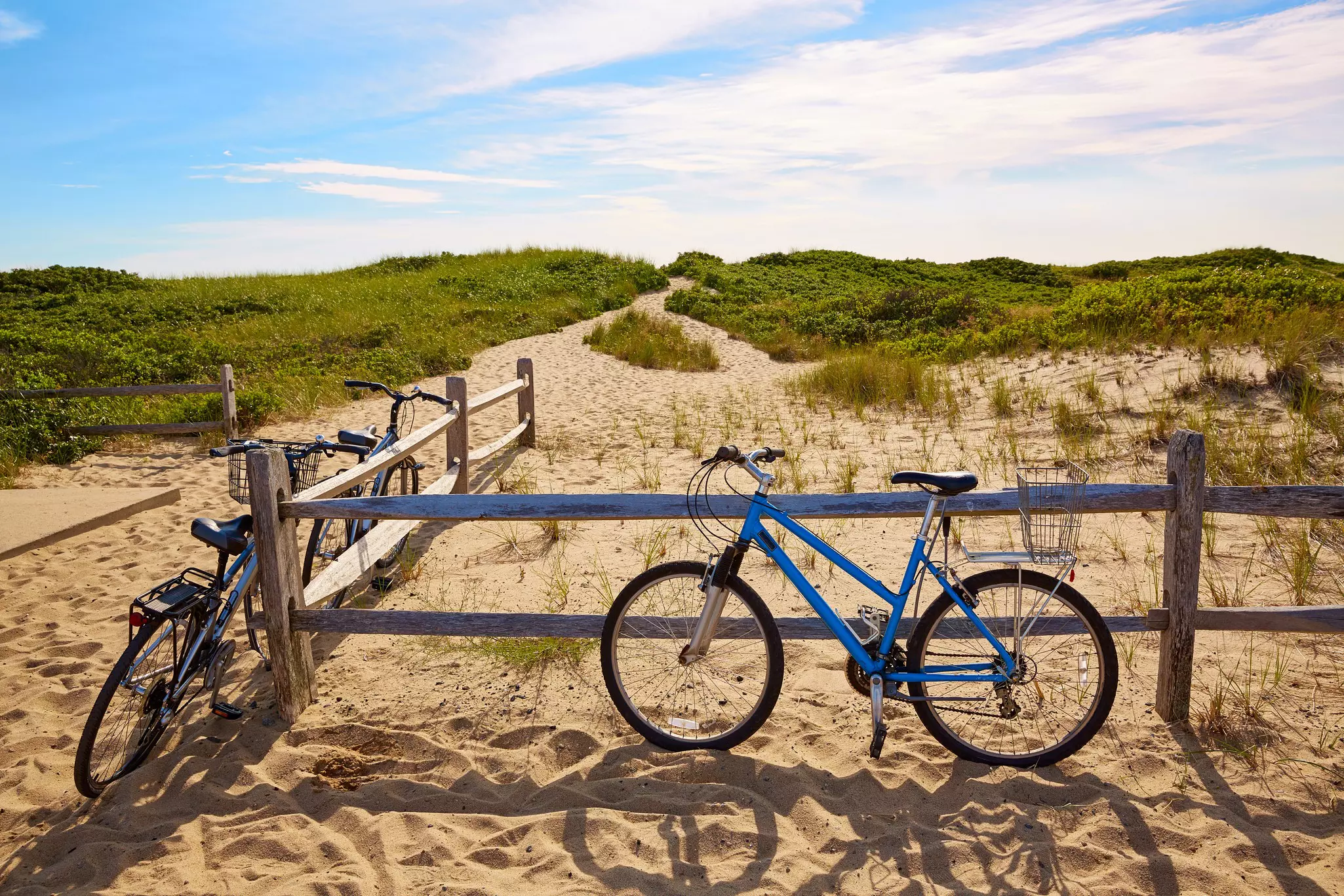 Bicycles rest against the wooden posts of a fence by sandy dunes.