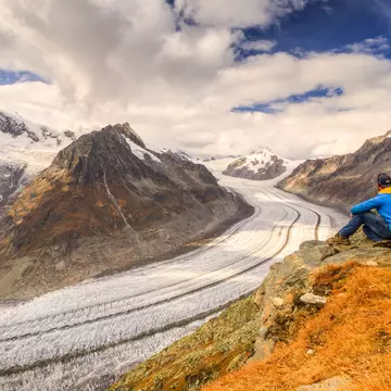 A hiker sits down and takes in the vast Aletsch Glacier as it snakes around the mountains in the Alps