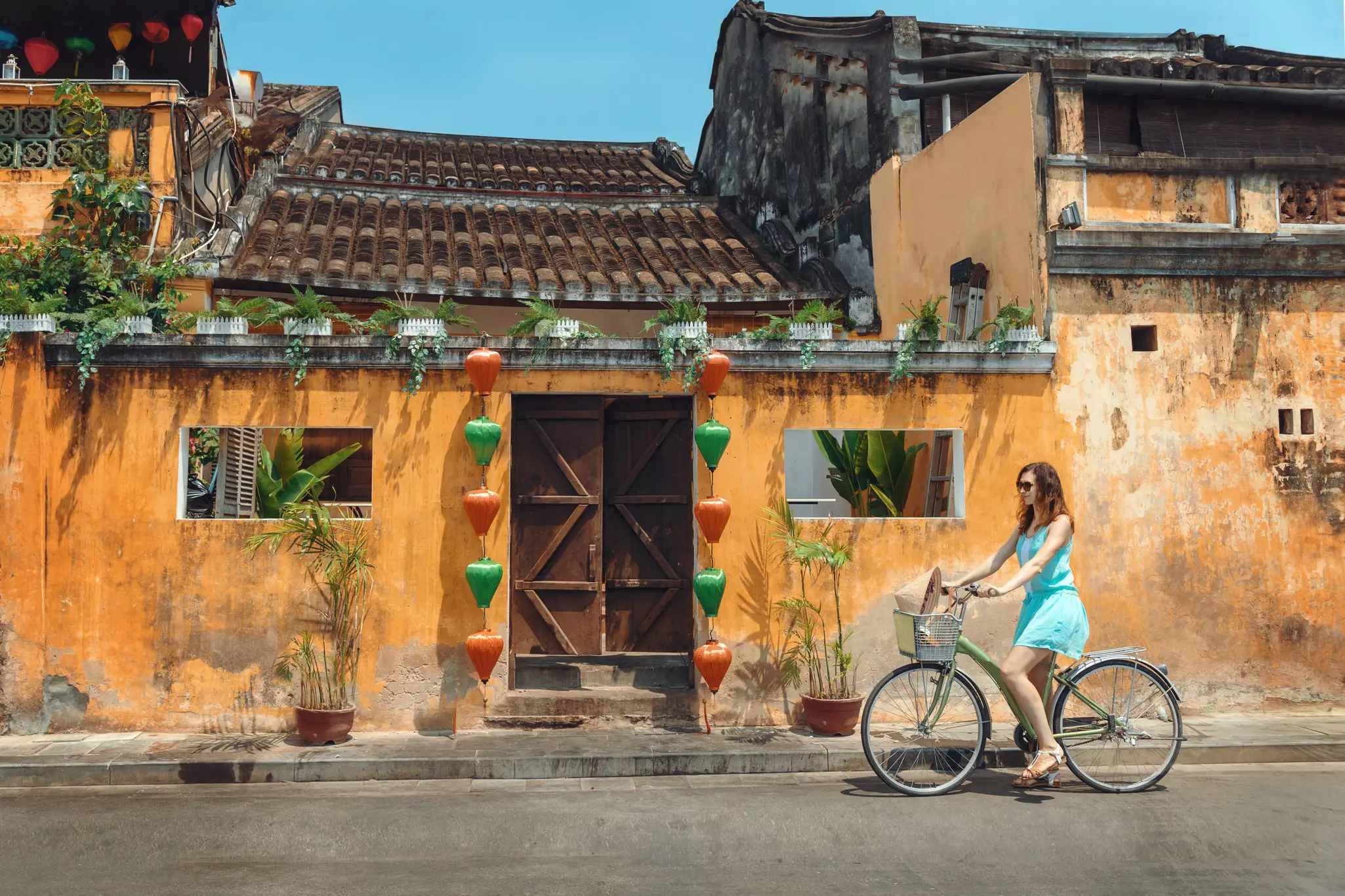 A woman wearing a blue dress riding a bicycle along the streets of Hoi An
