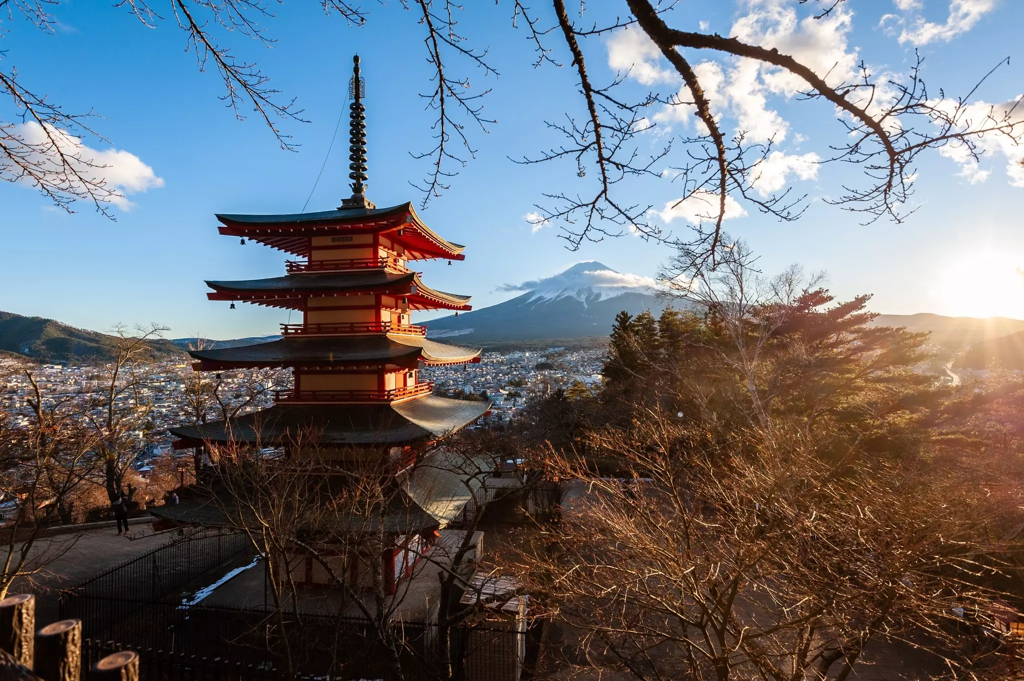 A snow-capped volcano is seen in the distance behind a tiered pagoda next to trees.
