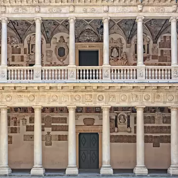 Two storeys of a stone colonnaded courtyard, its walls densely covered with carved coats of arms, a balustraded gallery running between them.