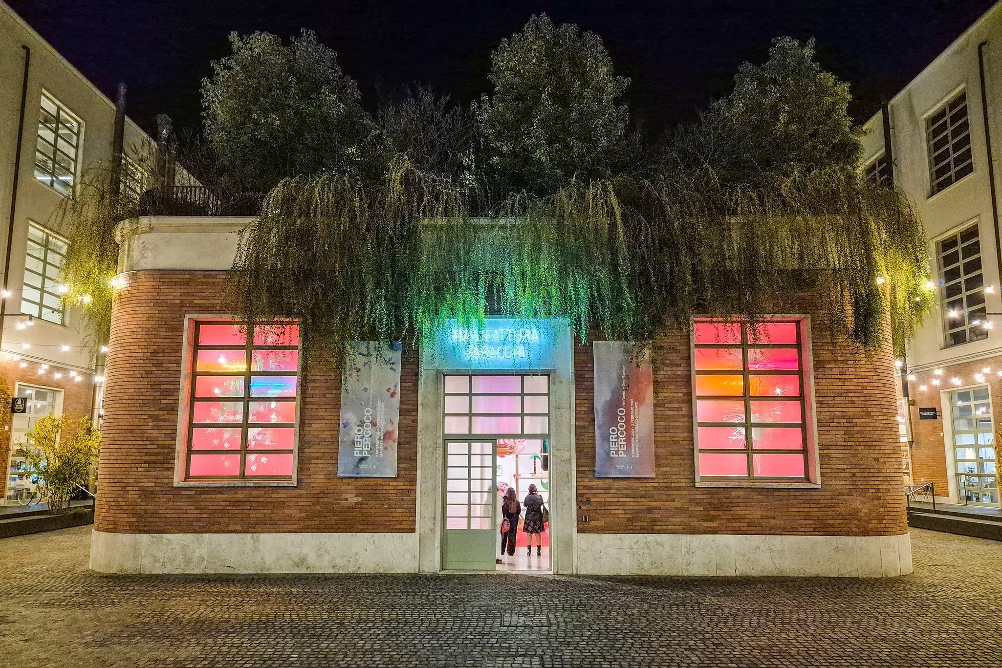 A renovated former industrial building contains displays of contemporary art featuring neon lights. Trees and bushes grow on the roof of the building.