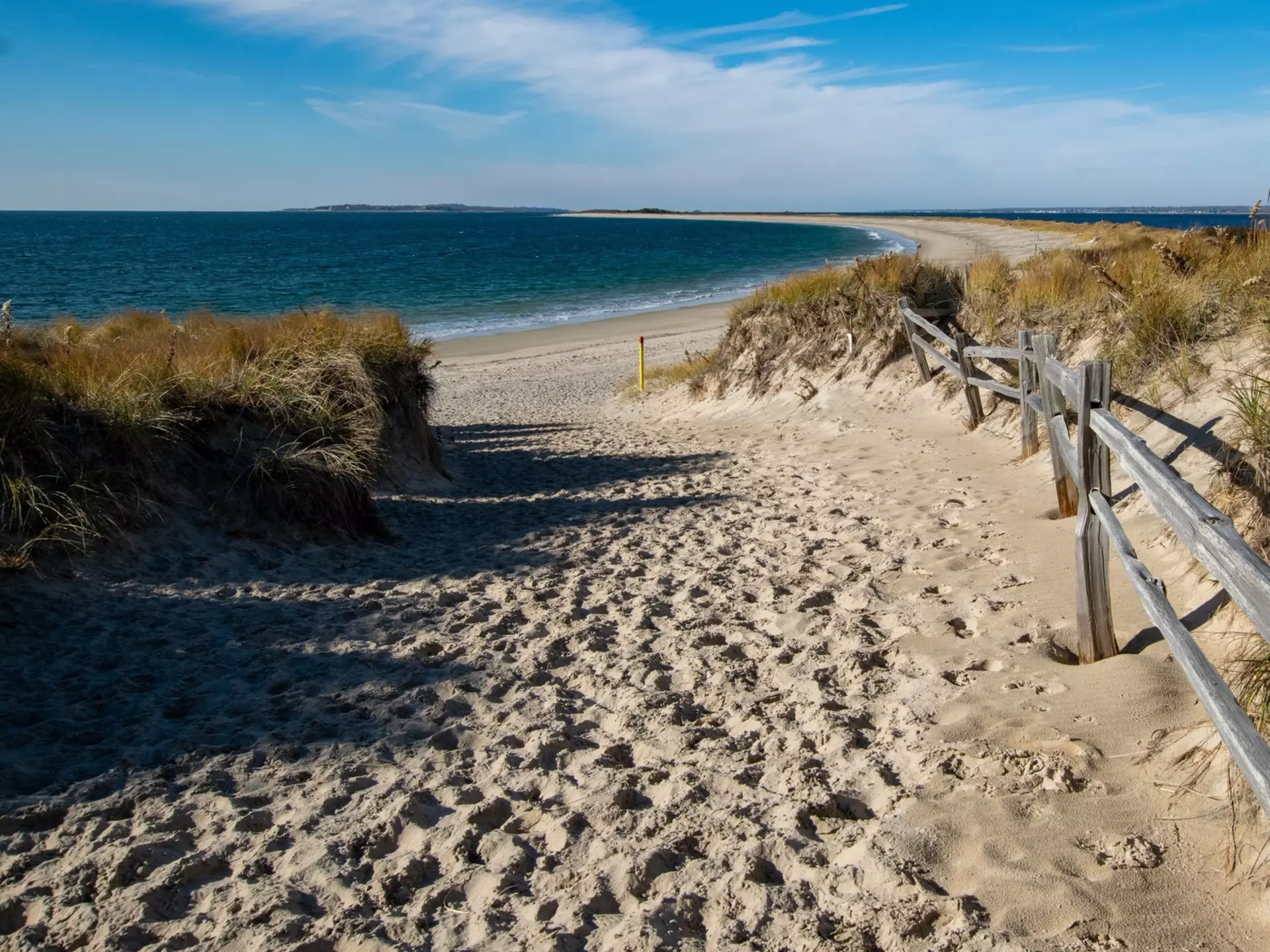 A sandy path between dunes to a beach.