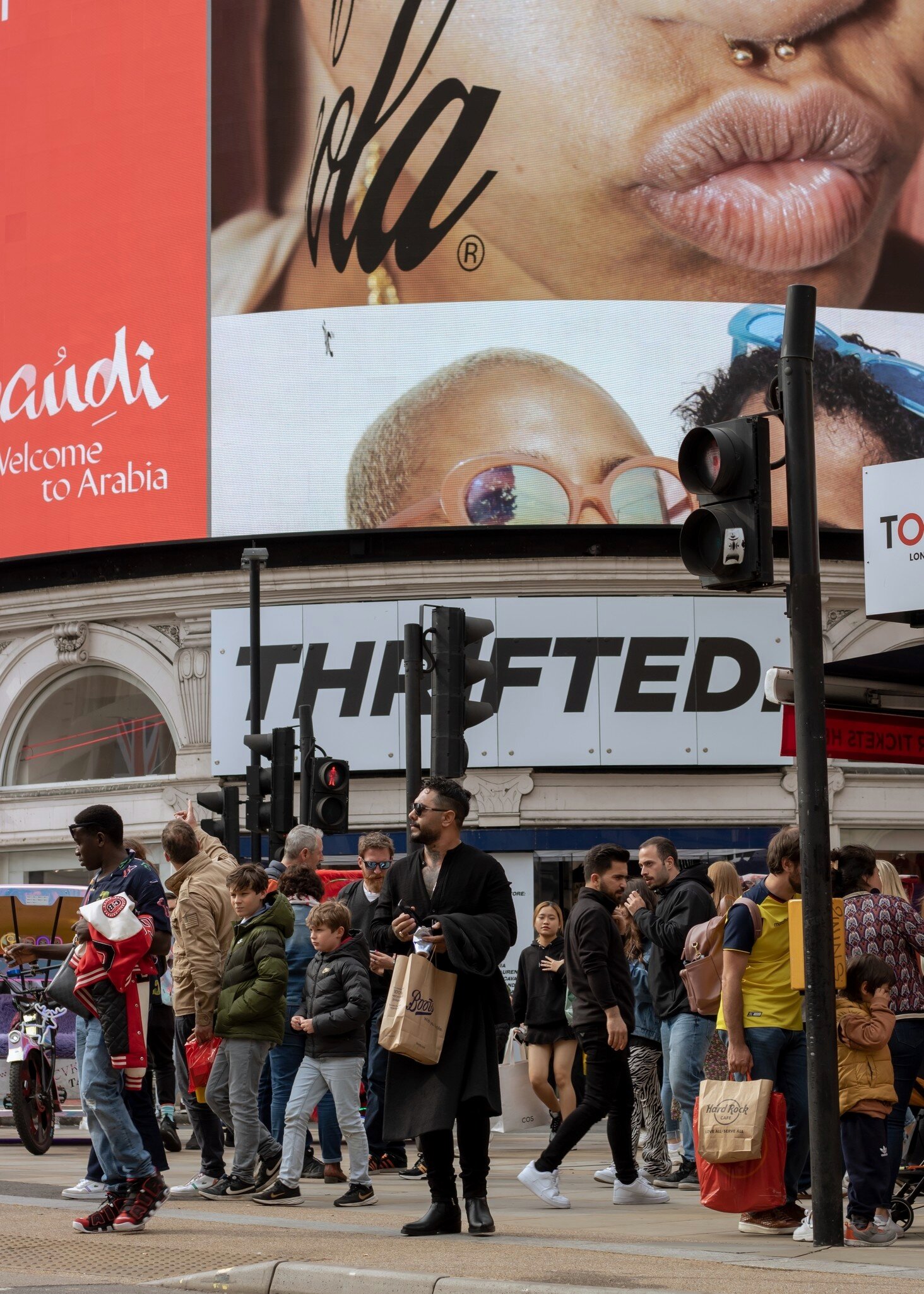 People in Piccadilly Circus waiting to cross the road, with advertising screens behind in London, UK.