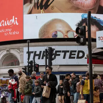 People in Piccadilly Circus waiting to cross the road, with advertising screens behind in London, UK.