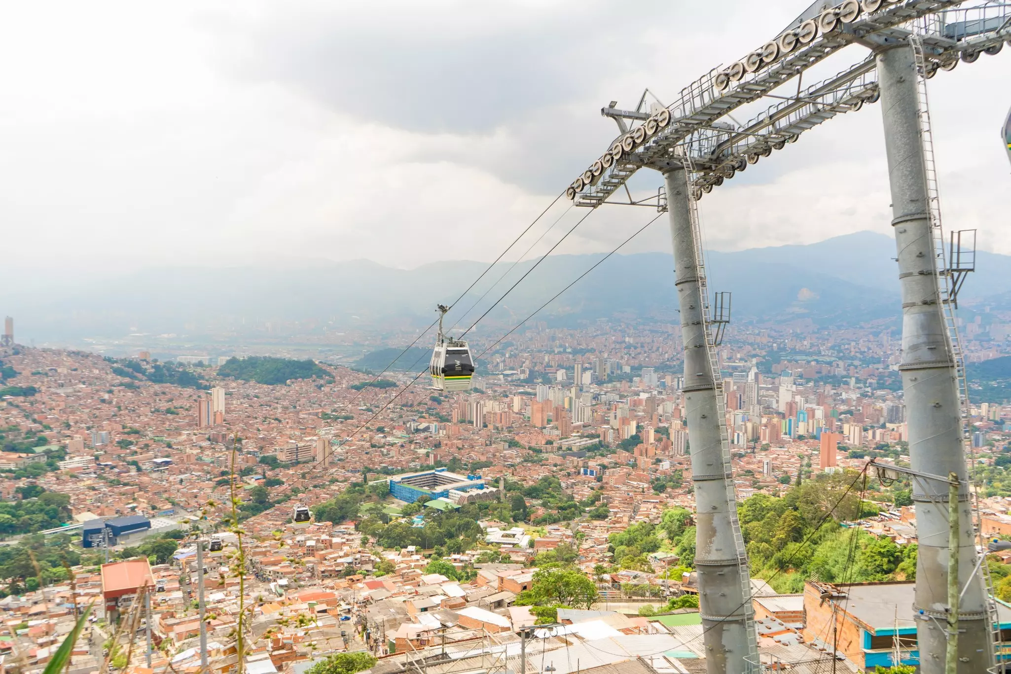 A cable car rises above a densely packed city with red roofs and high-rise buildings 
