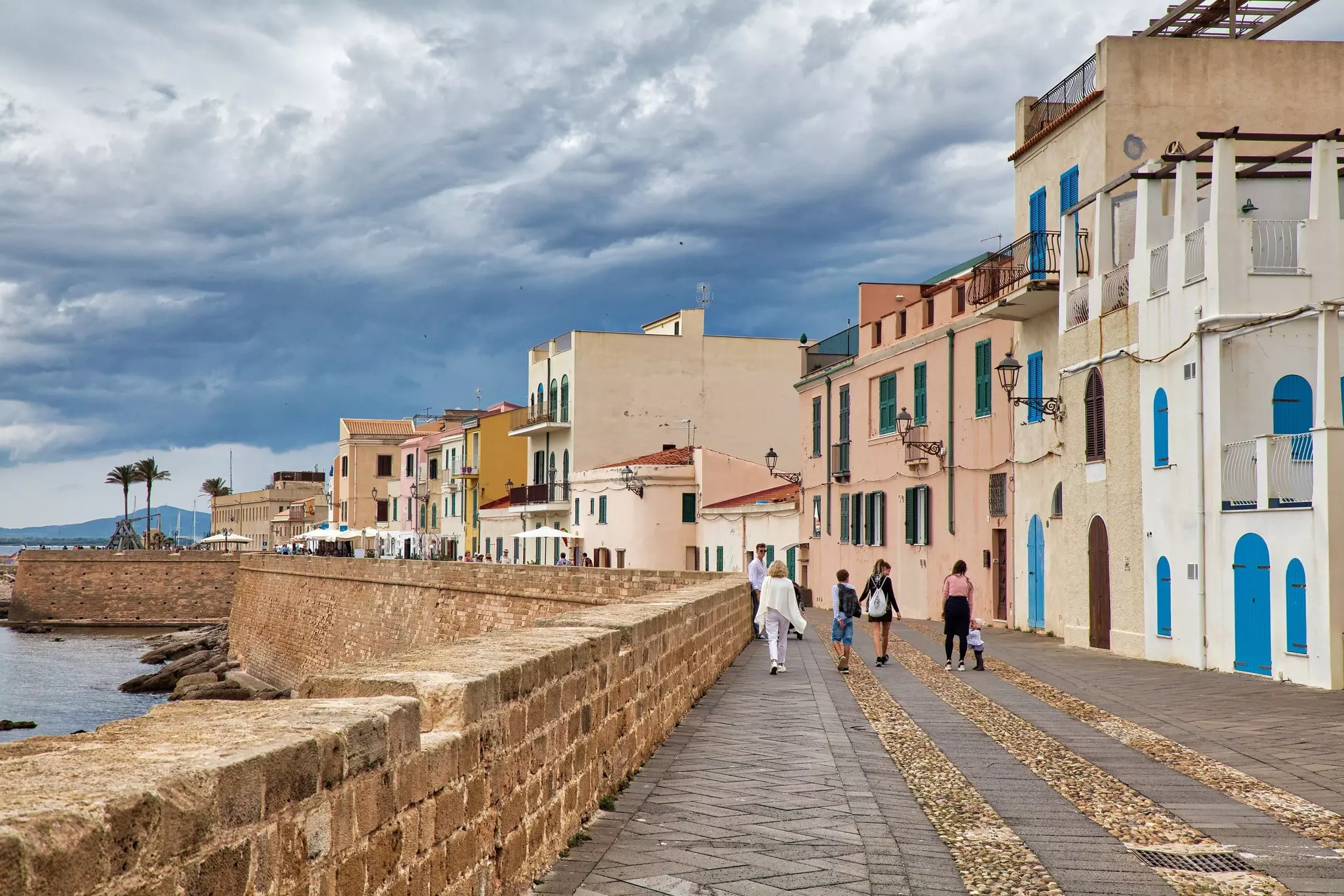 ALGHERO, ITALY - MAY 29, 2023: People walk along the seawall waterfront in rainy weather Alghero town in Sardinia island, Italy.