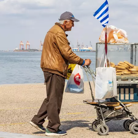An older man selling food from a cart on a waterfront