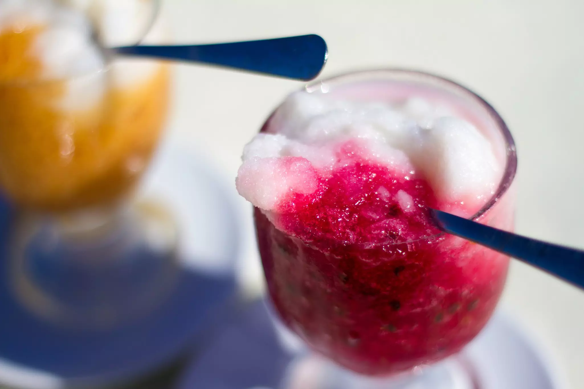 A spoon scooping out bright pink flavored ice from a glass.