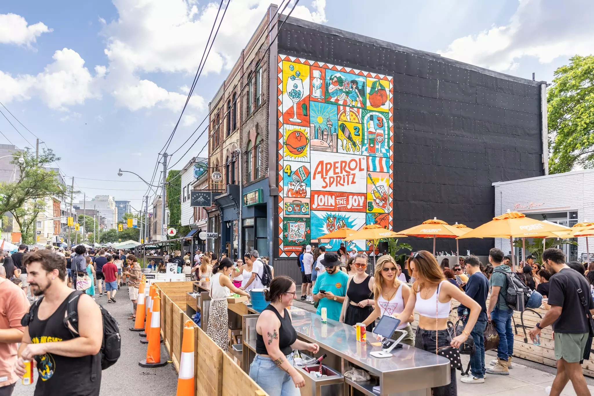 People gathered at a crowded street bar with orange umbrellas 