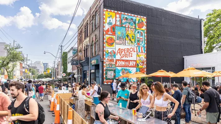 People gathered at a crowded street bar with orange umbrellas 
