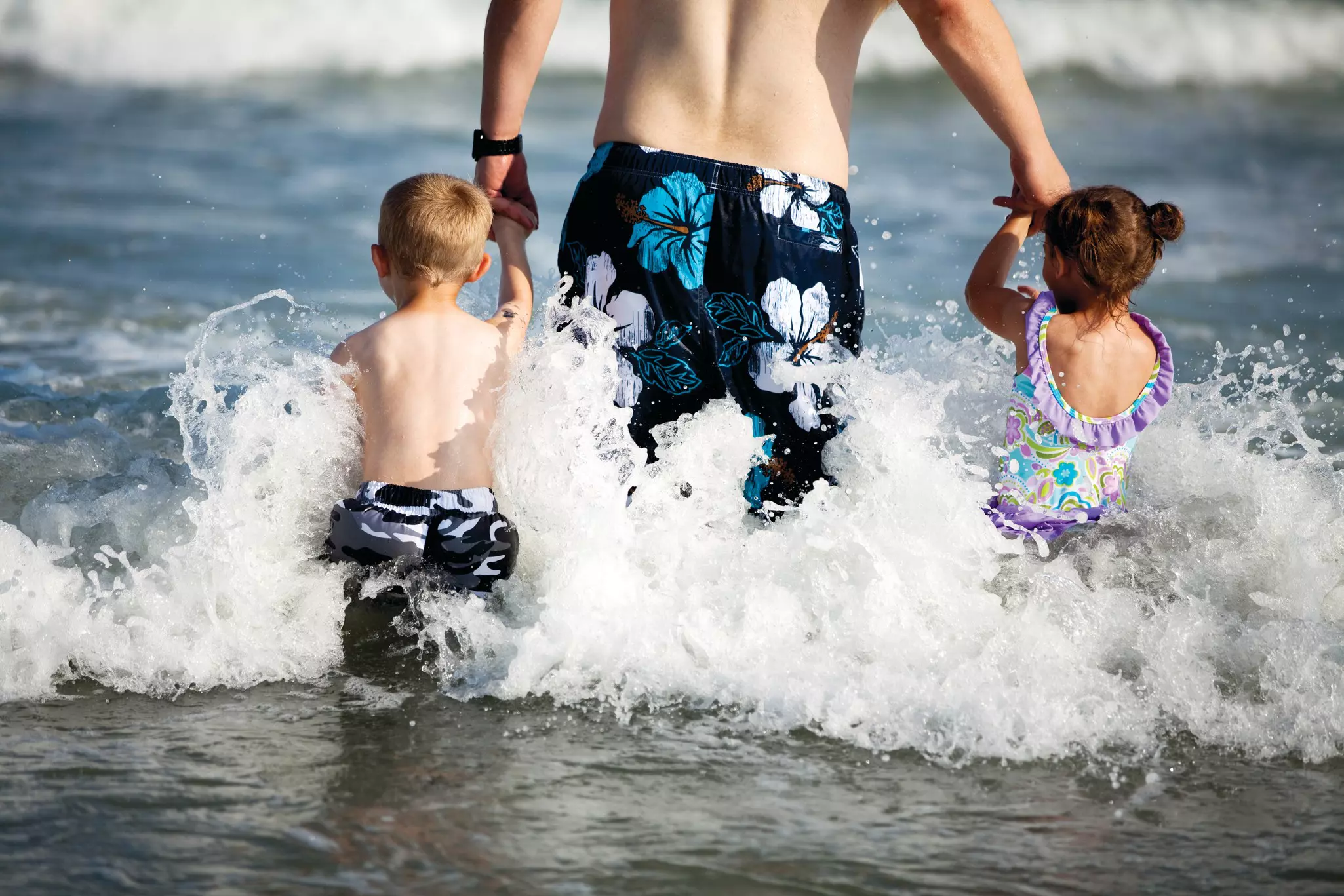 A father and a little boy and little girl head into the water at Myrtle Beach, South Carolina