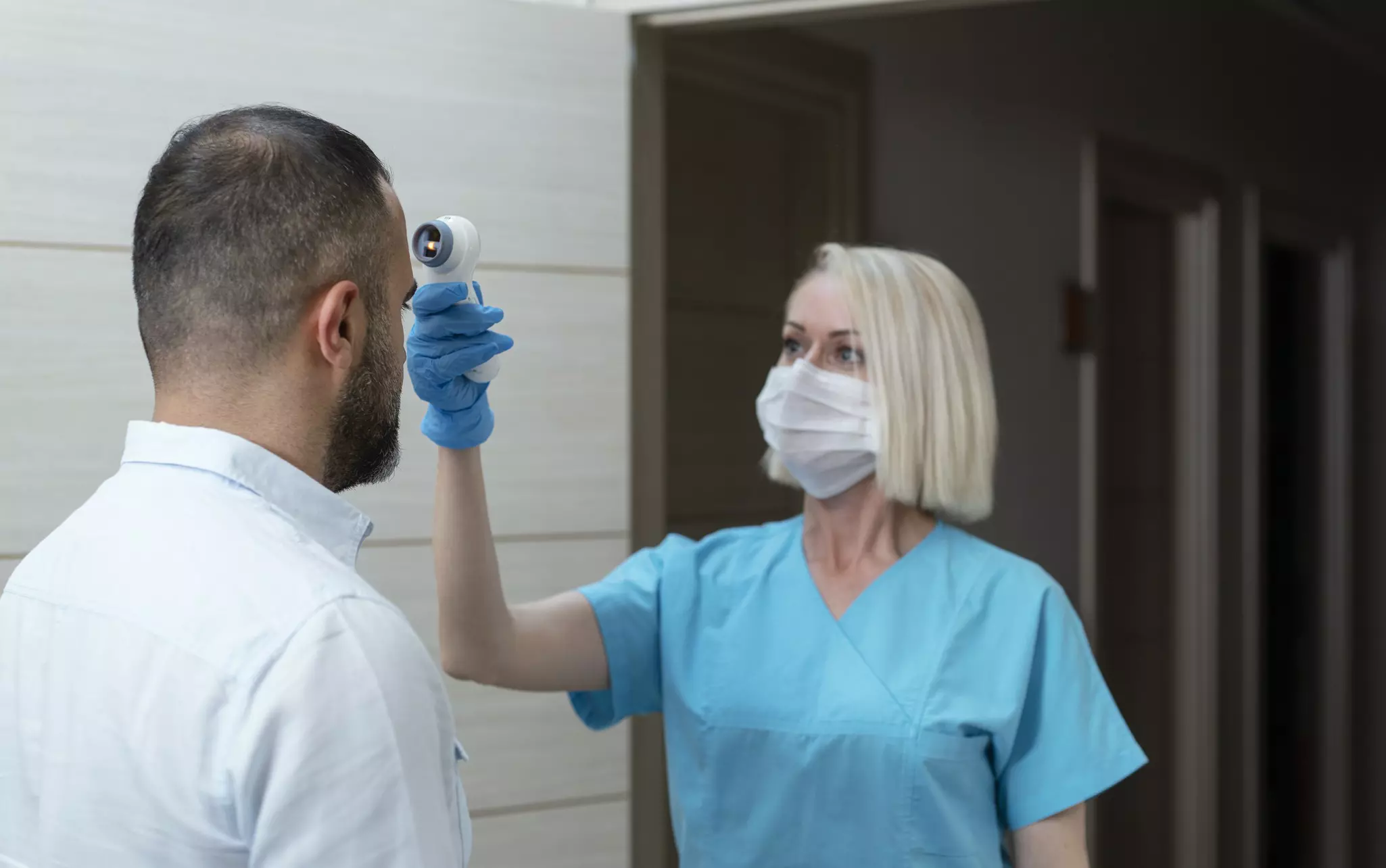 A doctor checks temperature at patient with infrared tool in hospital.