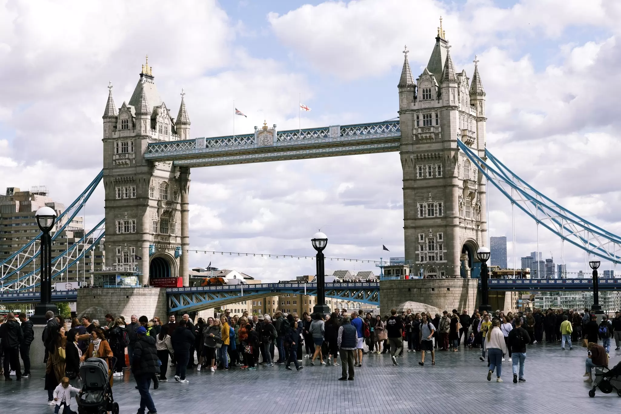 Large crowd of people standing in front of London Bridge. 