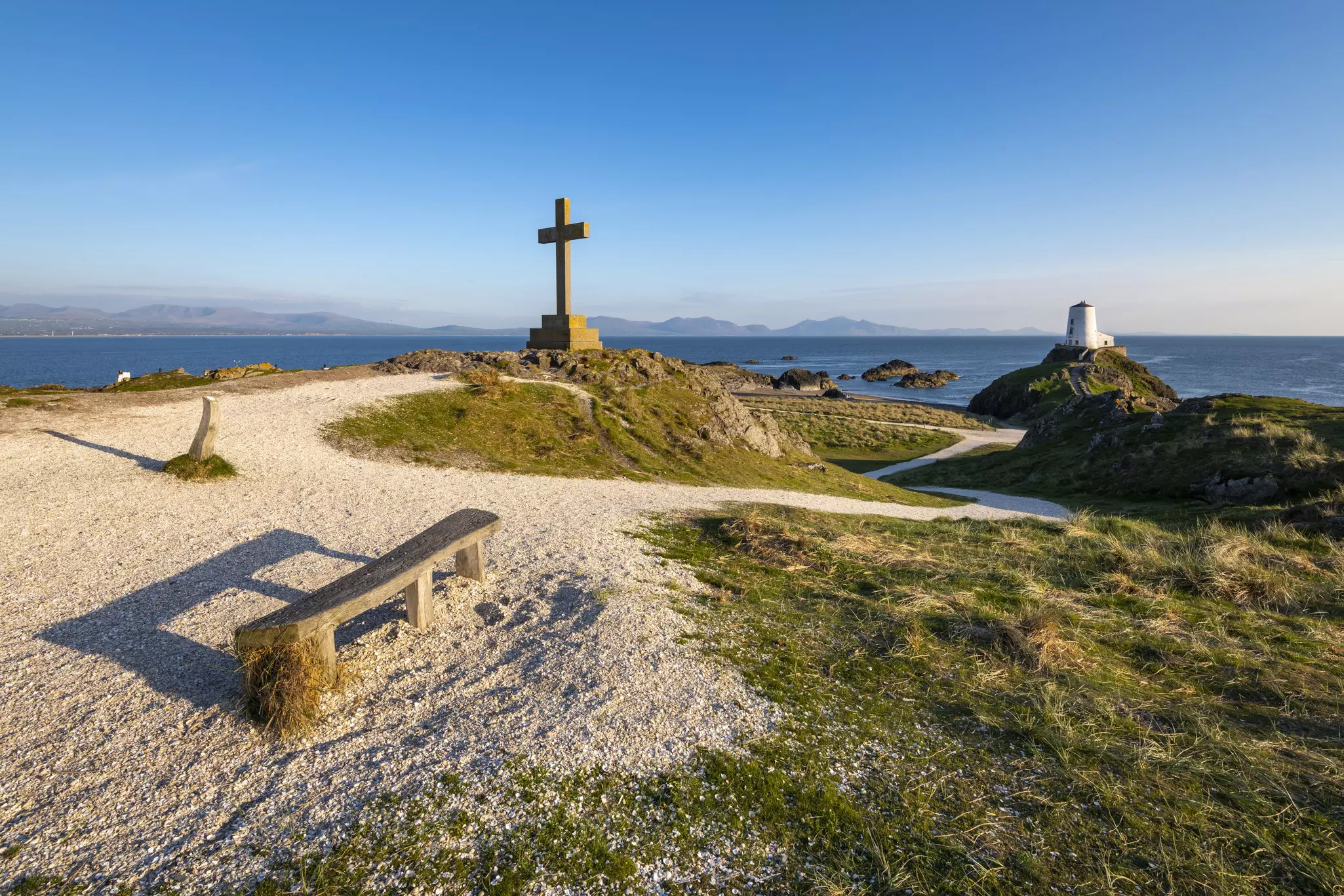 Stone cross and bench on a footpath to a lighthouse.
