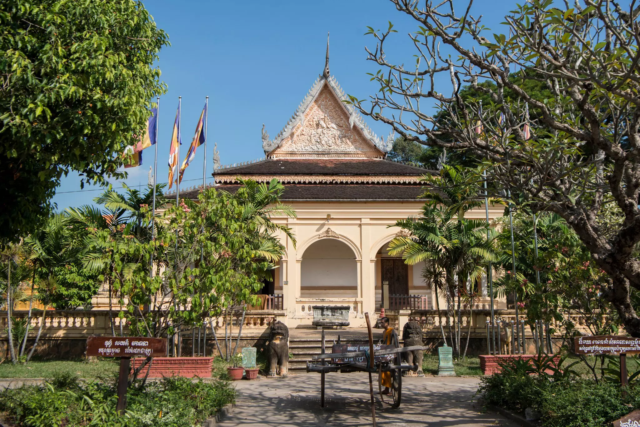 A small temple with flags and courtyard surrounded by trees on a sunny day.